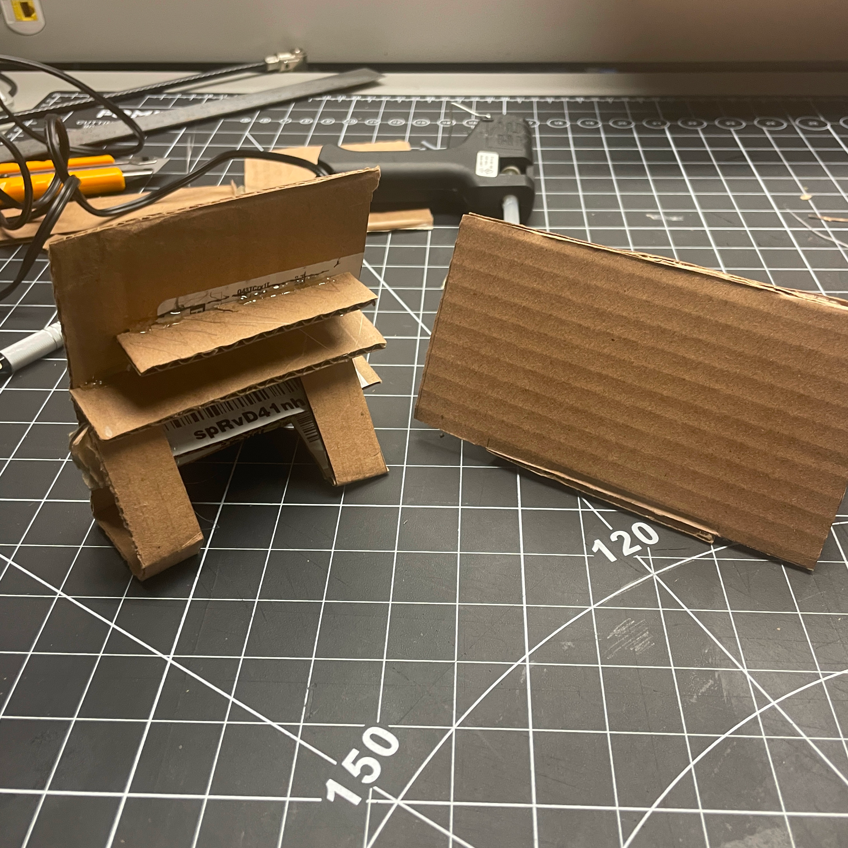 This is an image of the back of both phone stands. The main iterations we made improved on the stability and adjustability of the stand. First we included a lip at the front of the stand to help support the phone in place. Next, we added arms and extra panels to the back of the stand to allow the user to adjust their viewing angle.